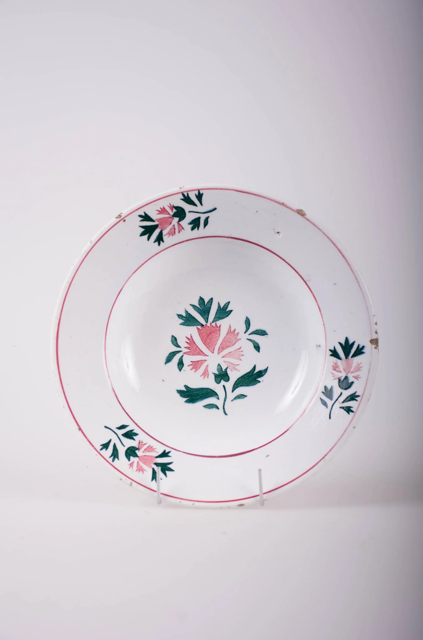 Farfurie de formă tronconică, adâncită; pe fund are găuri pentru agățare. În centru și pe margine este decorată cu motive fitomorfe și florale; pe margine sunt trei flori cu frunze încadrate de două cercuri concentrice; în interior este doar o floare cu frunze. Cromatică: fond: alb; motive: vișiniu; verde.