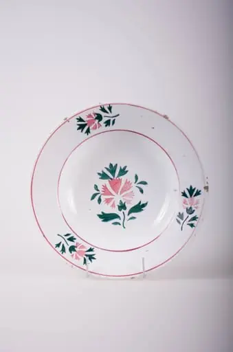Farfurie de formă tronconică, adâncită; pe fund are găuri pentru agățare. În centru și pe margine este decorată cu motive fitomorfe și florale; pe margine sunt trei flori cu frunze încadrate de două cercuri concentrice; în interior este doar o floare cu frunze. Cromatică: fond: alb; motive: vișiniu; verde.