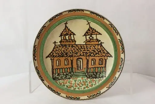 Vas de formă rotundă, cu pereții evazați, smălțuit în interior, decorat pe suprafața interioară, în prim-plan apărând un motiv arhitectural (biserică cu două turle); pe margine, două brâie de culoare ocru și verde și o succesiune de valuri (segmente), dublate de motive punctiforme. Pe partea exterioară apare semnătura de meșter (Stelian Ogrezeanu) și localizarea (jud. Vîlcea România). Cromatică: verde, cafeniu, maro, crem.
