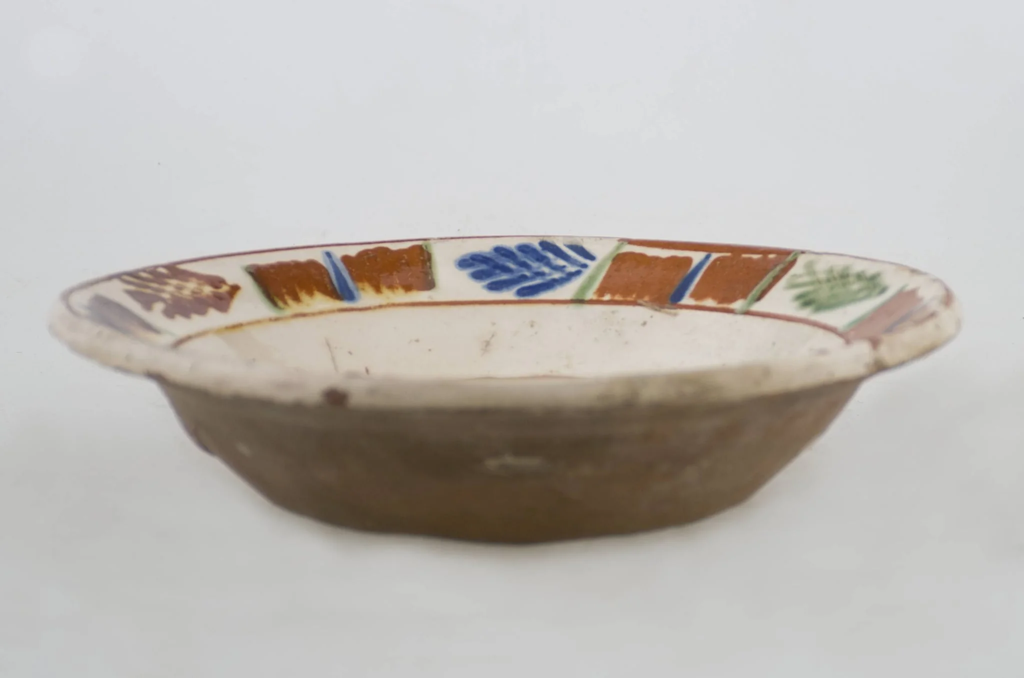 Vas ceramic de formă tronconică baza plată, pereții larg evazați și buza profilată. După modelarea la roată, uscarea și arderea recipientului, a fost aplicat un strat de angobă în interiorul vasului, peste care a fost pictat decorul floral și vegetal stilizat, format din două registre. În primul registru, situat pe fundul vasului și încadrat de o linie circulară, au fost realizate trei flori, cu petale albastre și mijlocul maro-roșcat, în jurul cărora se regăsesc petale verzi. Cel de-al doilea registru, cel care decorează buza vasului și este încadrat la rândul lui între două linii circulare, a fost decorat cu frunze și pete, despărțite de linii verticale. Cromatică: fond: alb; motive: maro-roșcat; albastru; verde., by Unknown, unspecified, 1850