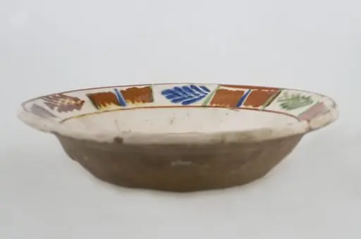 Vas ceramic de formă tronconică baza plată, pereții larg evazați și buza profilată. După modelarea la roată, uscarea și arderea recipientului, a fost aplicat un strat de angobă în interiorul vasului, peste care a fost pictat decorul floral și vegetal stilizat, format din două registre. În primul registru, situat pe fundul vasului și încadrat de o linie circulară, au fost realizate trei flori, cu petale albastre și mijlocul maro-roșcat, în jurul cărora se regăsesc petale verzi. Cel de-al doilea registru, cel care decorează buza vasului și este încadrat la rândul lui între două linii circulare, a fost decorat cu frunze și pete, despărțite de linii verticale. Cromatică: fond: alb; motive: maro-roșcat; albastru; verde.