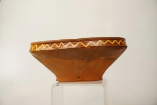 Farfurie adâncă de tip castron, cu fund îngust, corp tronconic și buză verticală, îngustă și ușor profilată. Decorul este pictat cu cornul, cu humă albă, direct pe suprafața neangobată a vasului și se compune din motive geometrice și floral-geometrizate: centrul farfuriei este decorat cu două cercuri concentrice de culoare albă, ce conțin între ele o linie circulară ondulată, iar în mijloc un element decorativ neregulat, de formă palmată, cu puncte albe în interior. Cinci motive aproximativ identice, formate din linii ovale cu puncte în interior și linii mici arcuite pe exterior, sunt pictate pe peretele vasului, pe exteriorul cercului ce marchează fundul acestuia, sugerând niște petale de floare. Patru pete de culoare verde-închis realizate completează decorul din această zonă. Buza farfuriei este decorată pe interior și pe exterior cu o linie circulară ondulată, de culoare albă. Suprafața ornamentată a farfuriei este acoperită cu un strat de smalț transparent. Cromatica: alb, verde-închis, pe fondul roșu al lutului ars.