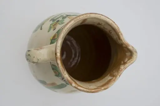 Cană bitronconică cu baza lată, pereții ușor bombați, ce se subțiază spre gât, lărgindu-se spre buză. Prezintă o toartă puternic arcuită. În partea opusă torții buza vasului are un cioc de scurgere. Decorații sub formă de șiruri de semicercuri dispuse concentric la baza gâtului și sub buză. . Motiv central pe pântecul vasului; o pasăre cu ciocul îndreptat spre o creangă cu frunze; un cal sau un cerb ce are pe spinare o lalea și în bot o frunză. Cromatică: fond: alb; cromatică: verde; galben; maron.