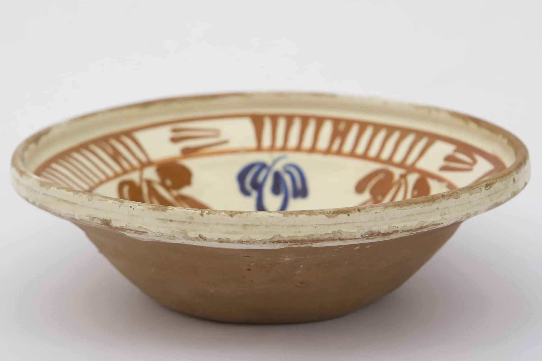 Piesă ceramică de dimensiuni medii, smălțuit la interior, având formă tronconică, cu baza plată, pereții ridicați și buza evazată. Întreaga suprafață interioră a piesei a fost decorată cu motive geometrizante și fitomorfe stilizate. O floare, cu petale verzi, roșii și albastre și cu un punct roșu în mijloc, este mărginită de un brâu circular, compus din opt reprezentări florale, cu aceiași cromatică. Marginal, pe buza piesei a fost realizat cel de-al doilea registru: două linii circulare, care încadrează patru registre, compuse din linii verticale, despărțite de alte patru registre din linii orizontale (2-3 linii). Farfuria era folosită în gospodărie pentru decorarea interioarelor. Prezintă uzură funcțională. Cromatică: fond: cărămiziu (exterior); crem (interior); motive: roșu; albastru; verde., by Unknown, unspecified, 1850