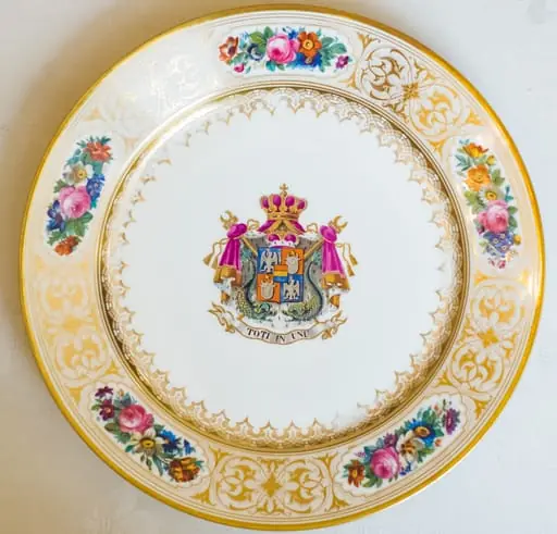Farfurie, model decorativ stil Louis-Philippe, ales pentru serviciul de masa de peste 100 de piese Cuza, comandat la manufacturile regale din Sevres. Acesta urma să fie folosit de familia domnitoare Cuza în palatul de la Cotroceni. Farfuria este întinsă, circulară, pictată pe margini cu cinci medalioane florale care alternează cu arabescuri aurii. Este decorată central cu stema Principatelor Române și deviza unionistă „Toți în Unu". Stema și motivele florale se caracterizează printr-o vie policromie: galben, auriu, nuanțe de roșu, roz, verde și albastru. Pe reversul ei apar două marci în câmp circular: „Chateaux de Trianon" (culoare roșu carmin) și „Sevres 1846" (cu albastru). De asemenea, se remarcă cartelul care conține, în cifre latine, datele dublei alegeri a lui Al. I. Cuza ca principe al Moldovei și Țării Românești.