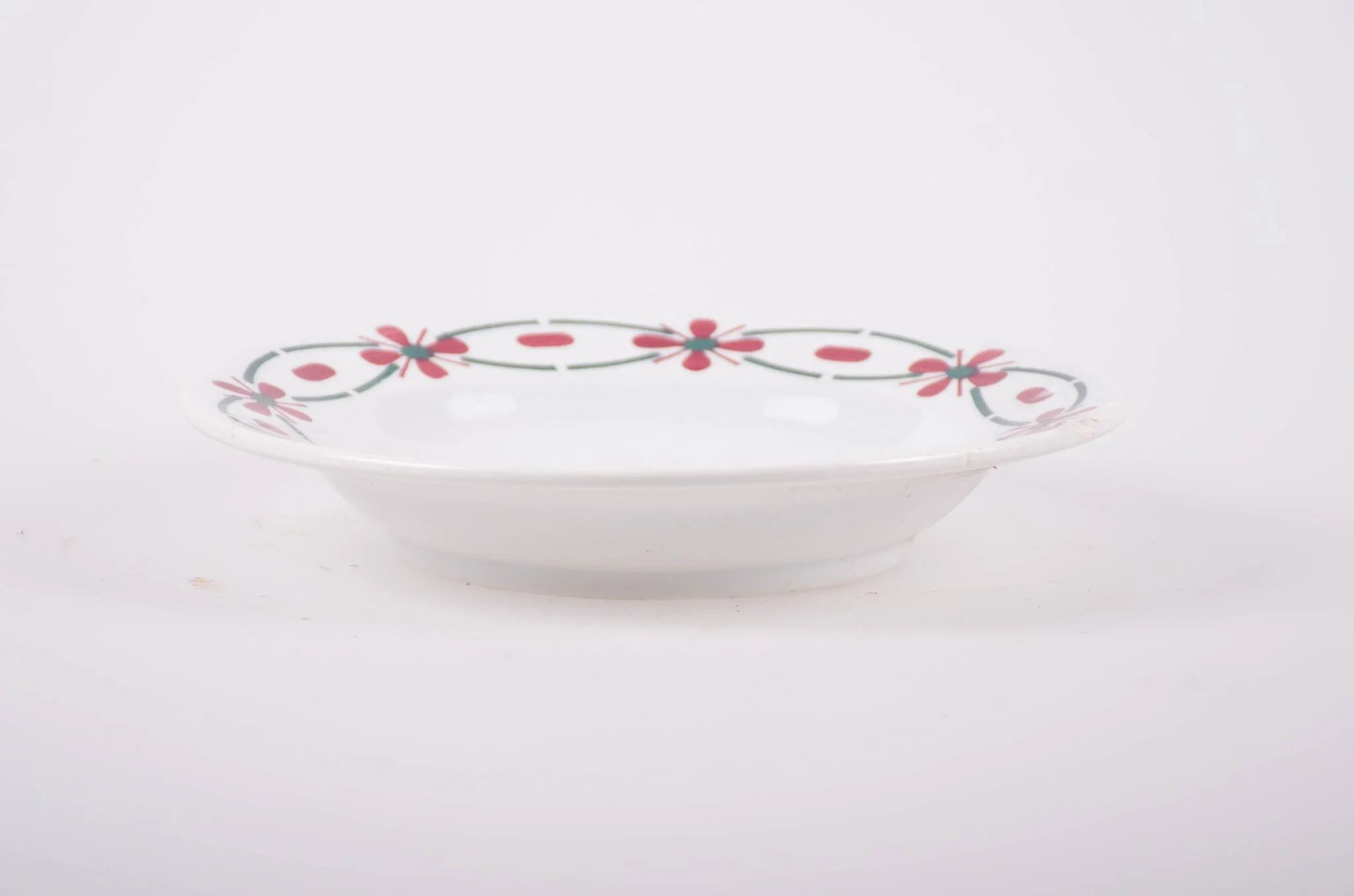 Farfurie din porțelan de formă tronconică. Pe fond alb, marginea este decorată cu flori stilizate. Cromatică: roșu și verde; interiorul farfuriei prezintă flori în: roșu; albastru; verde., by Unknown, 1950