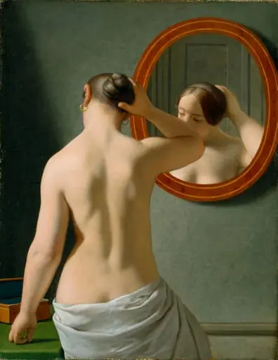 A nude woman doing her hair before a mirror