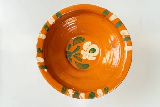 Farfurie adâncă, corpul de formă tronconică, cu buză îngustă, răsfrântă. Piesa este modelată la roata olarului, nefiind angobată. Decorul este realizat prin pictare cu pensula și constă în motive decorative florale (o floare cu frunze), dispuse central, pe fundul farfuriei și motive geometrice (linii groase, paralele), dispuse în trei registre, pe buza acesteia. Cromatica decorului: alb, verde. Farfuria este smălțuită pe interior, cu smalț transparent.