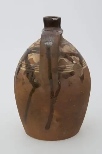 Ulciorul este realizat din ceramică. Pereții vasului sunt bombați și îngustați spre partea superioară unde se termină printr-un gât cu buza răsfrântă în exterior. Din partea superioară a gâtului aproape de buză pornește toarta vasului arcuită și prevăzută cu o "țâță". La baza gâtului și la diametrul maxim al ulciorului linii concentrice din angobă. Vasul este nears. Cromatică: maro deschis, maro închis, alb.