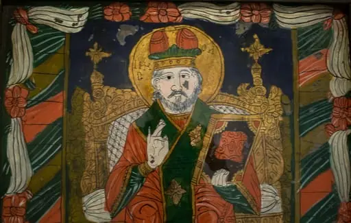 Icoana este pictată în oglindă, pe o foaie de glajă de formă dreptunghiulară în ax vertical. Sfântul Nicolae redat ca arhiereu, așezat pe un tron aurit, ține Evanghelia închisă în mâna stângă în timp ce cu dreapta binecuvintează. Evanghelia este de dimensiuni mari, redată în spațiu, cu margini aurite și decorațiuni roșii pe fond bleumarin. Sfântul ca Mare Arhiereu, poartă mitră înaltă, bipartită, omofor mare, verde intens decorat cu cruci aurite, stihar albastru , mânecuțe aurite, sacos roșu cărămiziu cu galon aurit la gât, mâneci și poale. De ambele mâini are atârnată câte o bederniță care are doar desenul schițat pe fondul sacosului. Chipul este sobru, barba albă, scurtă, părul scurt, ondulat. În jurul capului are un nimb aurit pe care este scrisă dezordonat inscripția. Tronul, de factură vădit barocă, are spătarul înalt, cu lemnul aurit, cu sculpturi abundente,(motive fitomorfe stilizate și motive geometrice) Spătarul este tapițat cu alb, decorat cu o rețea de linii întretăiate. Sfântul stă cu picioarele pe un postament de piatră. Câmp verde intens în partea de jos, albastru ultramarin în registrul superior. Pe laturile verticale este pictată câte o bandă lată, cu vrâste oblice în culori alternante: verde, auriu, roșu. Întreaga compoziție este încadrată de un chenar realizat dintr-o draperie albă stilizată strânsă din loc în loc cu flori roșii,la colțuri cu ghinde roșii. Desenul este caligrafic, fin, foarte minuțios, vădit inspirat din miniatura manuscriselor. Compoziția este echilibrată, paleta cromatică sobră(alb, albastru, roșu, verde, gri), armonioasă, rezultată din combinarea culorilor complementare cu auriul foiței. Rama este alcătuită din patru șipci drepte, îmbinate oblic la colțuri, colțul stâng jos fiind întărit cu un cui metalic. Culoare brun închis. Dosul- lemn subțire de brad, fixat pe spate cu bucăți de piele.