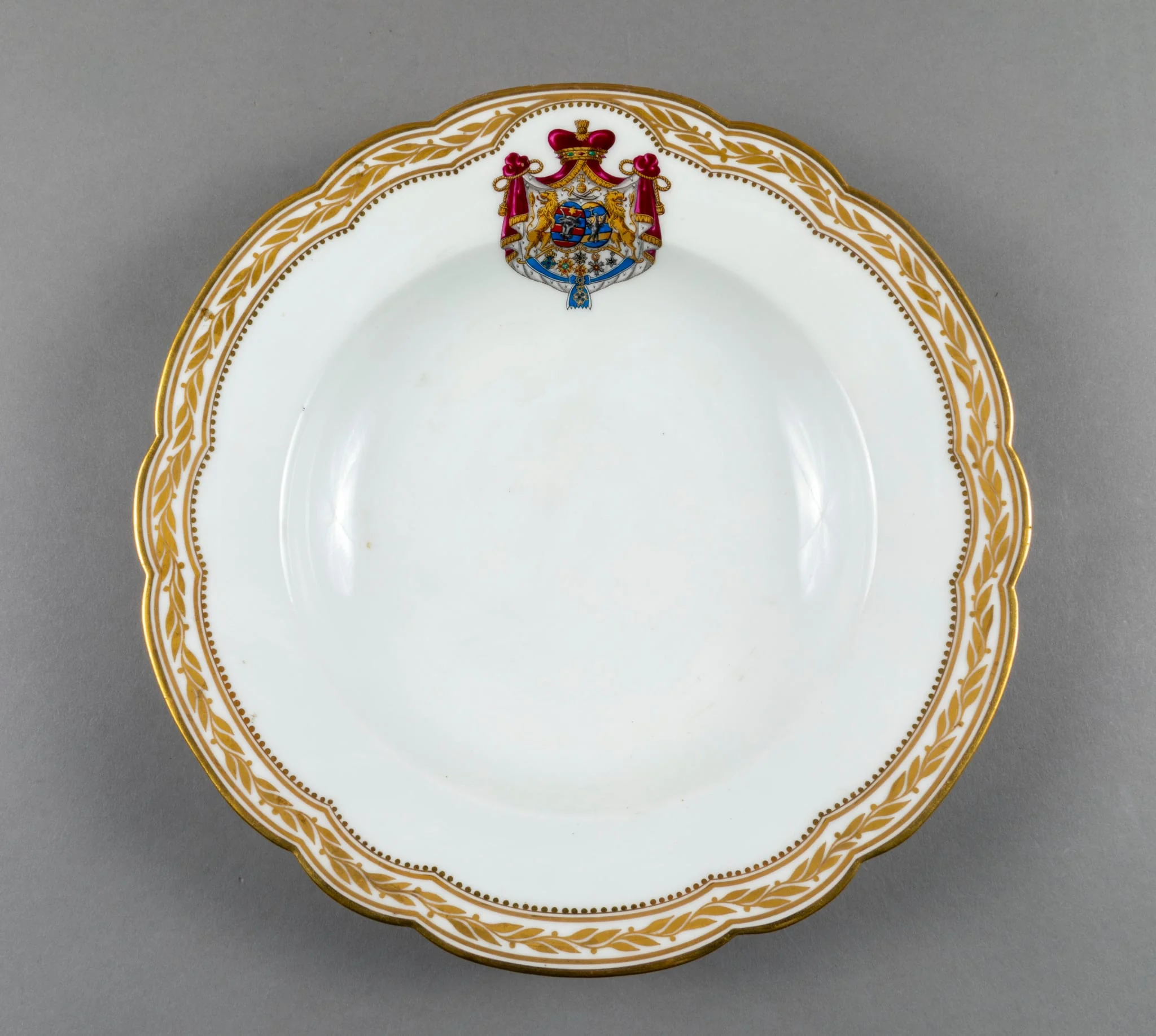 Farfurie adâncă de porțelan de Sevres, realizată din porțelan alb, cu margini treflate, decorate cu frunze de laur pictate, în centrul decorațiilor având blazonul familiei Suțu. Blazonul a fost adesea confundat cu cel al Principatelor Unite, fiind format din: stemele celor două țări românești: prima cea a Moldovei, cea de-a doua cea a Țării Românești, steme plasate pe două scuturi ovale, în fascie, acolate, puțin suprapuse, cea a Moldovei având capul de bour de argint cu stea în șase colțuri de aur, pe un scut cu segmente verticale egale roșii și albastre; cea a Țării Românești având acvila cruciată de argint, cu crucea de aur, scutul având segmente verticale galbene și albastre. Cele două scuturi au ca tenanți doi lei aurii, deasupra armele familiei Suțu – iataganul și sabia, ambele aurii, precum, pe un pavilion de purpură căptușit cu hermină, brodat cu ciucuri de aur și prins într-o coroană cu pietre scumpe. Pe scut, în partea inferioară se află și decorațiile familiei Suțu. Familia Suțu a fost o familie fanariotă grecească, venită în principate în cea de-a doua parte a secolului al XVIII-lea, având trei domni în ambele țări Românești (Alexandru Suțu, Mihai Suțu și Grigore Suțu). Blazonul familiei poate fi admirat inclusiv pe clădirea Palatului Suțu, astăzi Muzeul de Istorie a Municipiului București. Farfuria are marca atelierului Sevres și modelul din anul 1844, precum și seria., by Unknown, 1850
