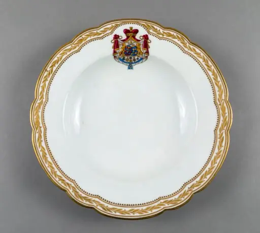 Farfurie adâncă de porțelan de Sevres, realizată din porțelan alb, cu margini treflate, decorate cu frunze de laur pictate, în centrul decorațiilor având blazonul familiei Suțu. Blazonul a fost adesea confundat cu cel al Principatelor Unite, fiind format din: stemele celor două țări românești: prima cea a Moldovei, cea de-a doua cea a Țării Românești, steme plasate pe două scuturi ovale, în fascie, acolate, puțin suprapuse, cea a Moldovei având capul de bour de argint cu stea în șase colțuri de aur, pe un scut cu segmente verticale egale roșii și albastre; cea a Țării Românești având acvila cruciată de argint, cu crucea de aur, scutul având segmente verticale galbene și albastre. Cele două scuturi au ca tenanți doi lei aurii, deasupra armele familiei Suțu – iataganul și sabia, ambele aurii, precum, pe un pavilion de purpură căptușit cu hermină, brodat cu ciucuri de aur și prins într-o coroană cu pietre scumpe. Pe scut, în partea inferioară se află și decorațiile familiei Suțu. Familia Suțu a fost o familie fanariotă grecească, venită în principate în cea de-a doua parte a secolului al XVIII-lea, având trei domni în ambele țări Românești (Alexandru Suțu, Mihai Suțu și Grigore Suțu). Blazonul familiei poate fi admirat inclusiv pe clădirea Palatului Suțu, astăzi Muzeul de Istorie a Municipiului București. Farfuria are marca atelierului Sevres și modelul din anul 1844, precum și seria.