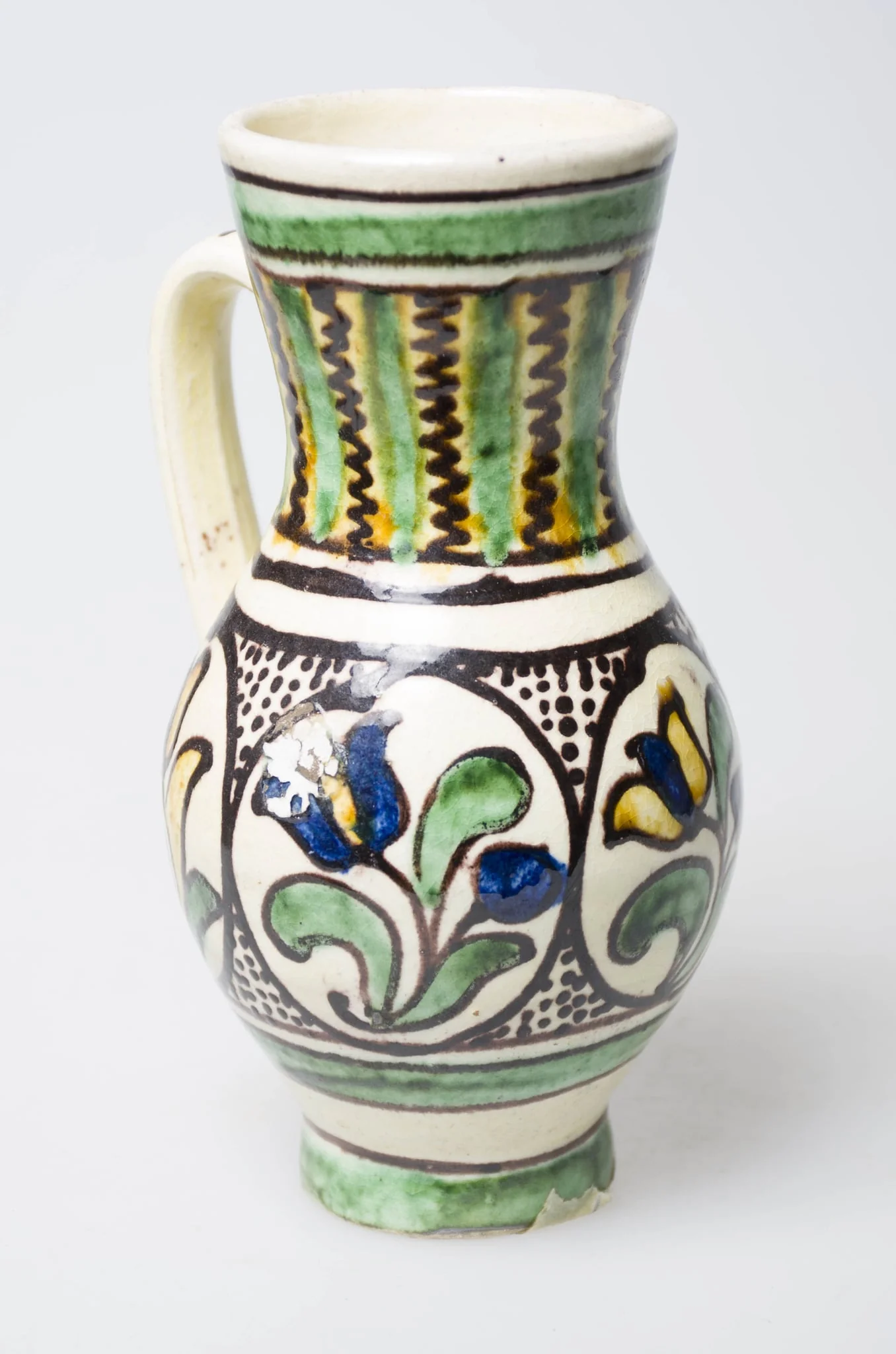 Recipient ceramic de formă ovoidală, smălțuit, cu gâtul lung, fund inelar și buza dreaptă. Prevăzut cu o toartă arcuită, care pleacă din mijlocul gâtului spre partea inferioară a vasului. Intens stilizat cu motive florale, vegetale și geometrice, pictate cu pensula, în două registre diferite. În primul registru, situat în zona gâtului, sunt pictate dungi late și linii meandrice dispuse pe verticală, alternativ. Aproape de gura vasului, sunt prezente dungi late și linii circulare. În al doilea registru întâlnim patru flori încadrate în cercuri și între acestea, puncte mici, umplând astfel cu decorații toată zona bombată a recipientului. Registrele sunt delimitate între ele de trei linii circulare. În partea inferioară, întâlnim ca și la gură, o dungă lată încadrată de două linii circulare. Prezent motiv geometric pe toartă sub formă de linie vălurită. Cromatică: fundal: alb; motive: galben; albastru; verde; maro închis.