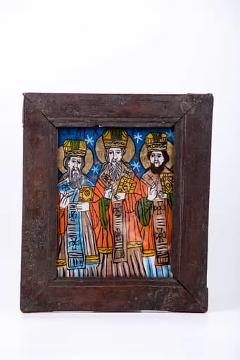 Cei Trei Sfinți Ierarhi Vasile cel Mare, Grigorie de Dumnezeu Cuvântătorul și Ioan Gură-de-Aur slujesc și săvârșesc Sfânta Liturghie împreună. Sunt înveșmântați în veșminte liturgice: sacos crem-albastru-alb-crem, felon roșu vermillon, epitrahil albastru-verde cu câte patru cruci negre. Sfântul Vasile cel Mare are Sfânta Evanghelie în mâna dreaptă. Sfântul Ierarh Grigorie de Dumnezeu Cuvântătorul Binecuvântează. Fondul registrului superior este cerul albastru-regal, bogat ornamentat cu elemente astrale - stele roșii și albe. Cromatica este luminoasă și armonioasă: verde văratic, alb, roșu vermillon, galben-ocru, bej, crem, albastru regal și bleu-ciel, negru. Este o icoană specifică picturii de Țara Oltului, cu un desen fin cu conturul negru și cromatica pastelată. Inscripția din româno-chirilică se traduce Vasile Grigorie Ioan.