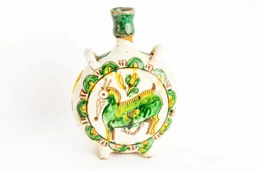 Ploscă circulară prevăzută cu două toarte în laterale pentru atașarea curelei. Fond alb. Pe fețele obiectului decorul este similar: un animal fantastic cu corp de culoare verde, cu contururi ușor zgrafitate, cu două coarne subțiri ușor ondulate de culoare maro deschis, cu un bot alungit, deasupra animalului este amplasată o lalea galbenă cu frunze galbene și verzi. Întreaga compoziție este înscrisă într-un cerc bordat de semicercuri de culoare verde cu interiorul galben. Pe muchia ploști sînt dispuse forme geometrice neregulate zgrafitate colorate în verde și respectiv galben. Gîtul ploștii este colorat cu verde.