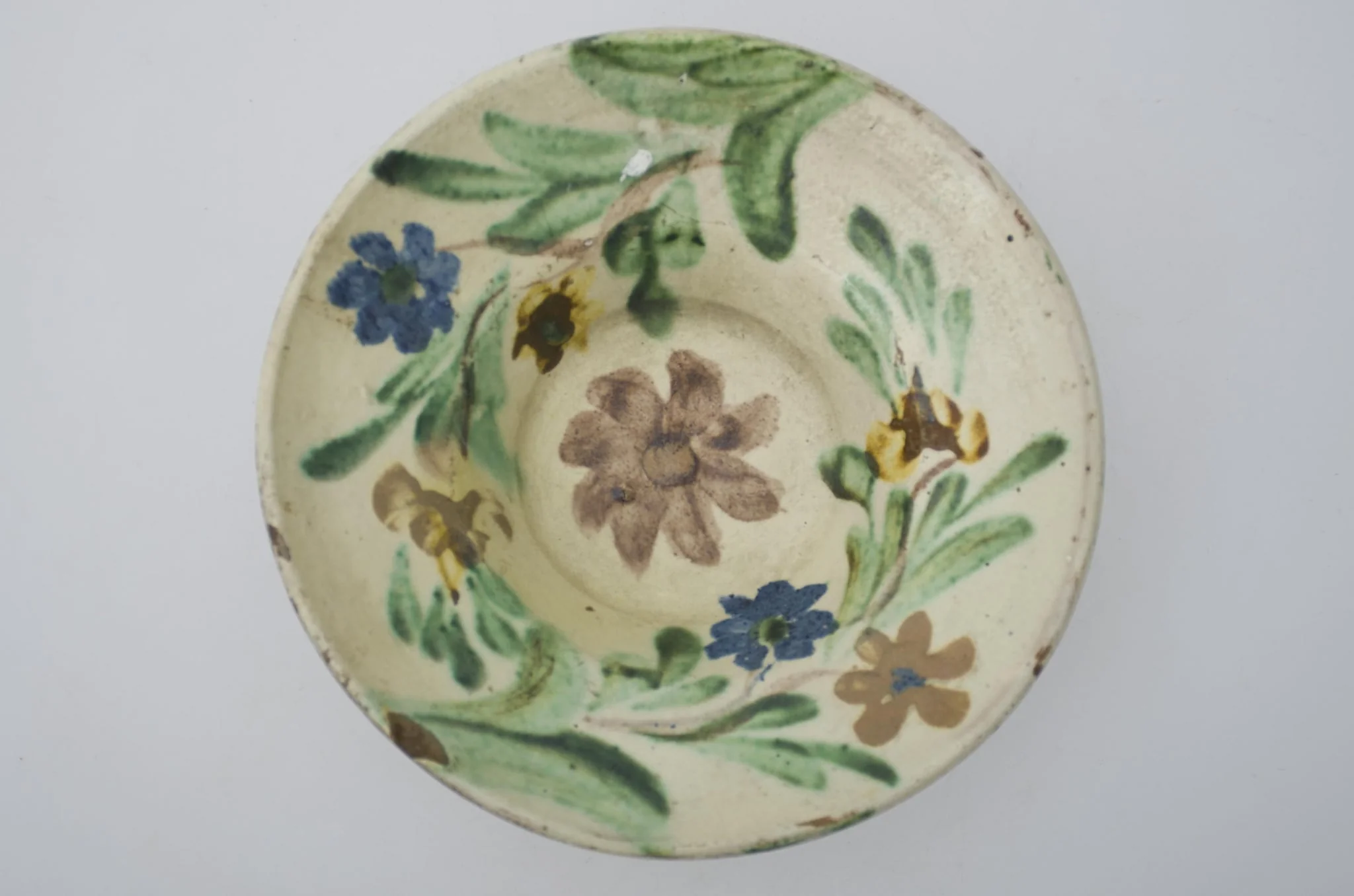 Farfurie cu marginea foarte lată și evazată, smălțuită în interior. Decor floral pe toată suprafața interioară. Cromatică: fond: alb; motive: brun; verde; galben; albastru., by Unknown, 1850