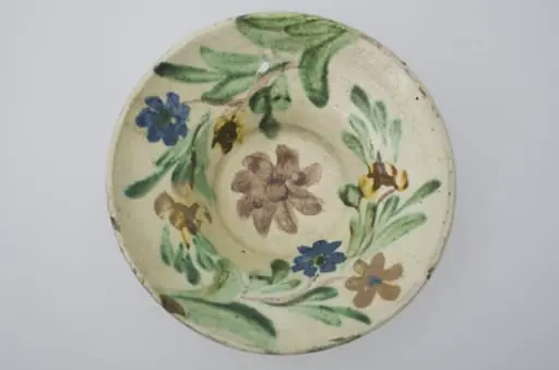 Farfurie cu marginea foarte lată și evazată, smălțuită în interior. Decor floral pe toată suprafața interioară. Cromatică: fond: alb; motive: brun; verde; galben; albastru.