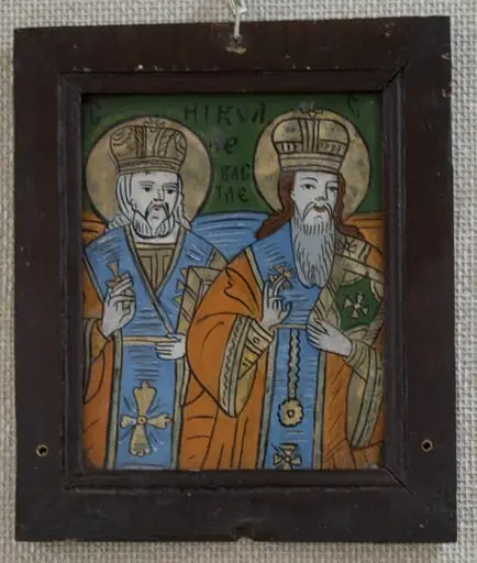 Icoana este pictată pe dosul unei bucăți de sticlă dreptunghiulară, în ax vertical; Sunt reprezentați sfinții ierarhi Nicolae al Mirelor Lichiei și Vasile cel Mare, într-o asociere mai puțin întâlnită. Cei doi sfinți sunt redați 3/4, din ușor semiprofil, privind către stânga lor. Cu dreapta binecuvintează cu degetul inelar unit cu cel mare, în stânga țin o carte sfântă la piept. Poziția este mai puțin uzitată: sfântul Nicolae este plasat puțin în spatele sf Vasile, creînd perspectivă. Ambii sunt înveșmântați cu sacosuri roșu cărămiziu cu borduri aurite, stihare orange cu mânecuțe, aurite, omofor bleu cu chenar și cruci aurite. Pe cap au mitre rotunde, înalte, bipartite. Sfântul Vasile are la gât un engolpion circular, confundat probabil cu o decorațiune. Sfântul Nicolae are barba scurtă, părul lung, alb, iar sfântul Nicolae are babrba lungă, albă și părul castaniu. Câmp verde întunecat, cu porțiuni de bleu și orange în dreptul umerilor sfinților, corespunzător culorilor veșmintelor. Inscripția este scrisă cu negru, cei doi S fiind plasați în colțuri,. Compoziția este ușor comprimată. Rama este alcătuită din patru șipci drepte, îmbinate oblic la colțuri, profilate pe o porțiune mică la interior, vopsite cu o culoare maron închis-roșcat, peste care s-a aplicat un lac lucios. Are trei găuri circulare, suscentral și lateral jos, pentru a fi prinsă oblic(mai târzii) Dosul este realizat din brad, fixate în cuie.