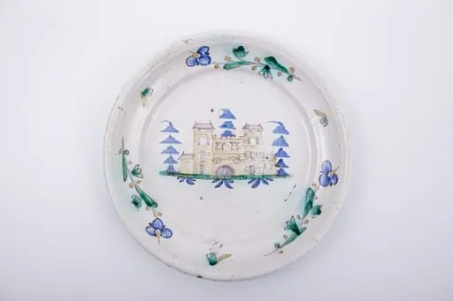 Farfurie plată,cu marginea lată și evazată spre interior. Marginea este decorată cu trei fire de floare de nu-mă-uita intercalate de un mic motiv fitomorf. Decorul central reprezintă un castel medieval poziționat într-un peisaj naturalist, înconjurat de trei brazi. Cromatică: alb, albastru, verde, maro.