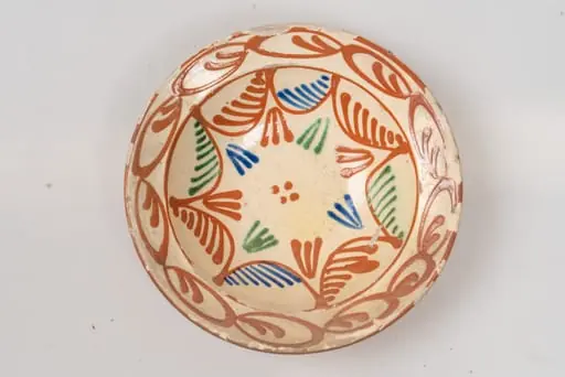 Farfurie adâncă, cu buză relativ îngustă, evazată; este acoperită pe suprafața interioară cu un strat de angobă albă, peste care este pictat cu cornul decorul format din motive geometrice: fundul farfuriei și peretele acesteia este decorat cu motive formate din linii curbe de culoare maro, ce au pe suprafața interioară linii oblice paralele, inegale ca mărime, de culoare verde, albastru, maro; grupuri de câte trei linii colorate, în formă de V și patru puncte centrale, de culoare maro. Buza farfuriei este decorată cu un șir continuu din motive formate din linii ovale, de culoare maro, cu câte două linii sub formă de virgulă în interior. Suprafața ornamentată a farfuriei este acoperită cu un strat de smalț transparent. Cromatica: alb, albastru, verde, maro.