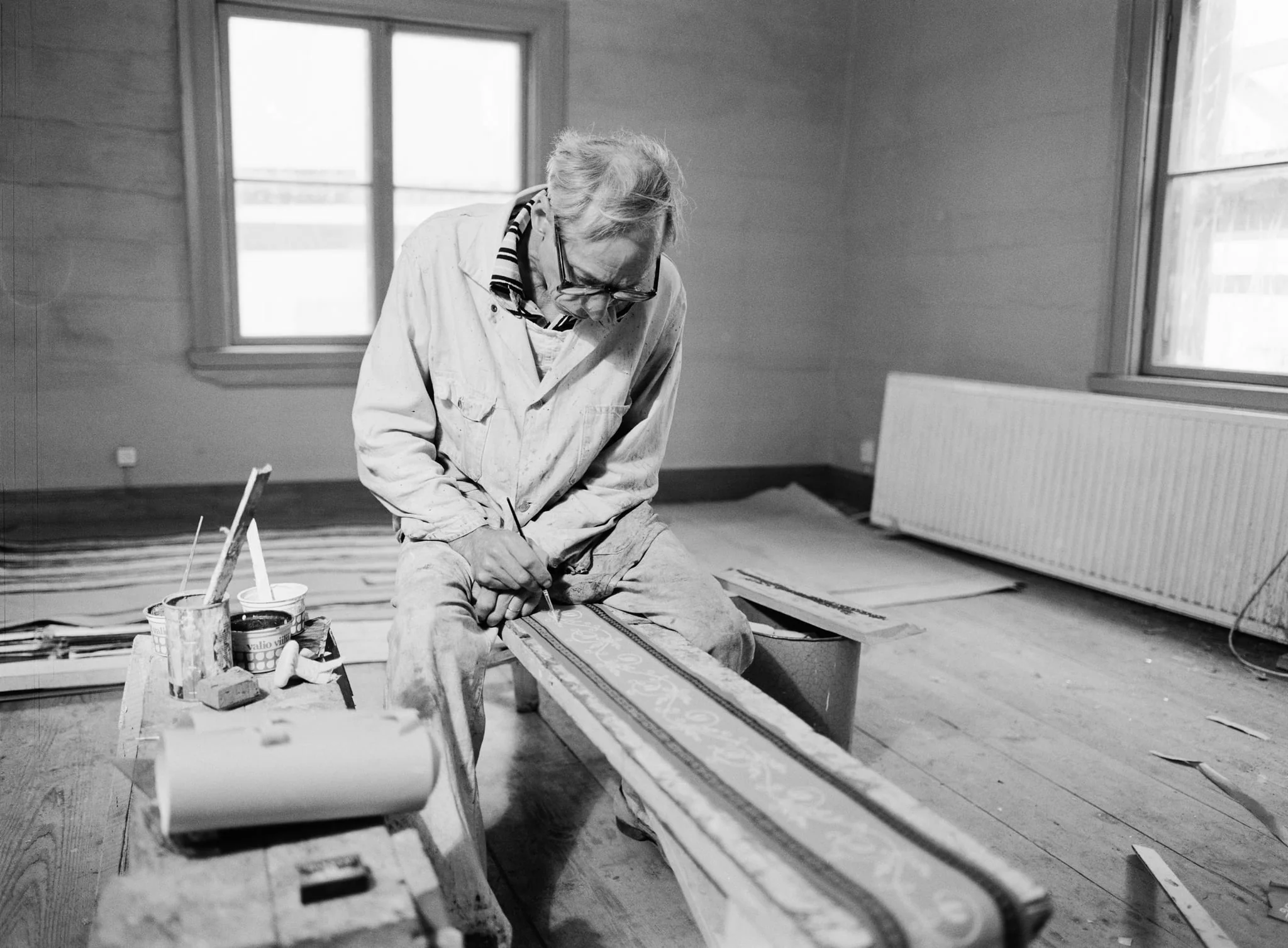Konservaattori Fjalar Hermansson istuu Ruiskumestarin talon salissa maalaamassa tapettiboordia., by Johnny Korkman, 1979