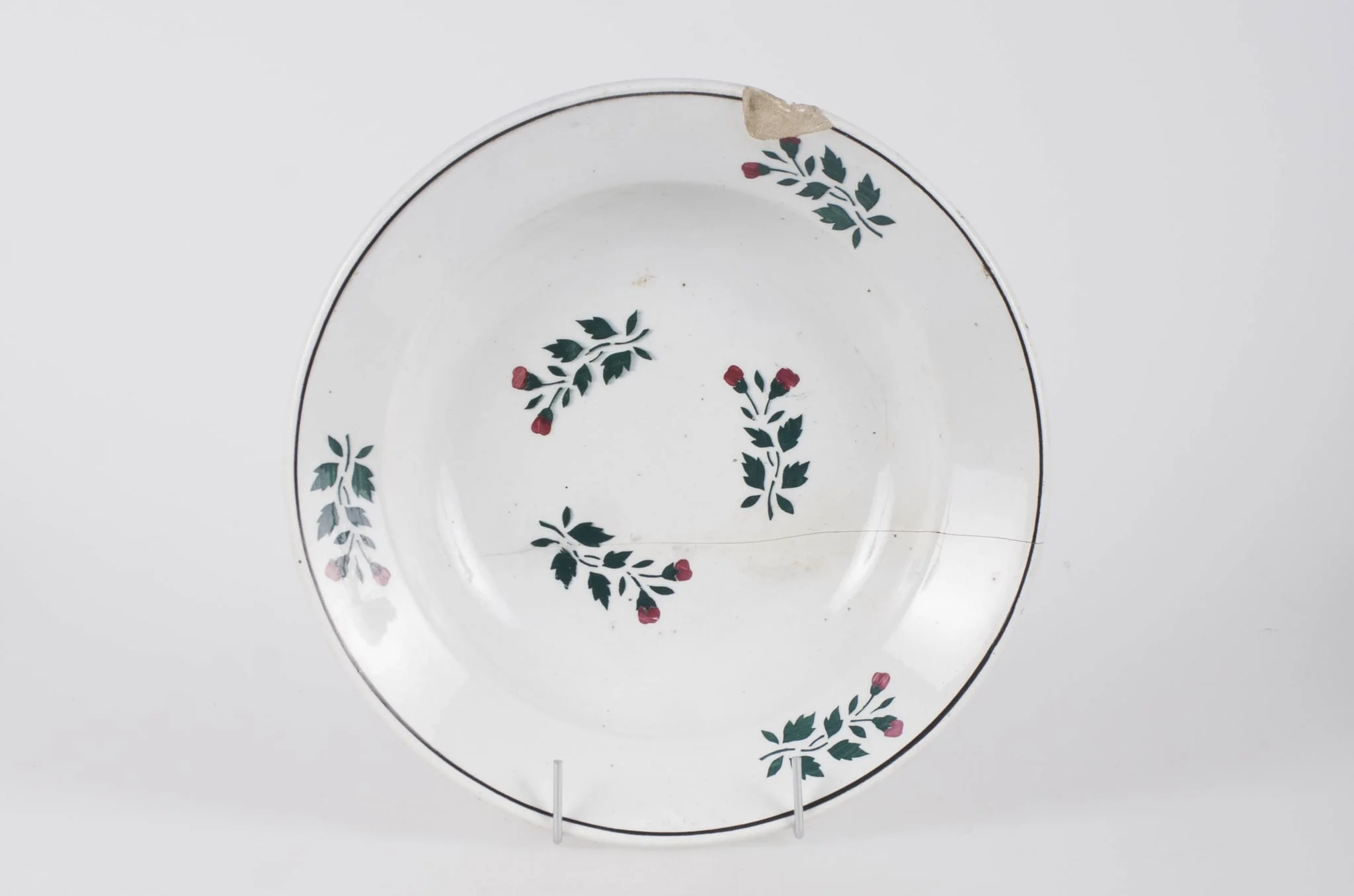 Farfurie din faianță smălțuită cu smalț alb. Vasul este de formă circulară, ușor adâncită. Pe fundul vasului decorul este floral-vegetal. Pe buza vasului se identifică trei flori, un decor geometric (cerc) ce încadrează decorul floral. Pe fundul vasului se identifică marca ”WILHELMSBURG”. Cromatică: fond alb; motive: verde; roșu., by Unknown, 1850