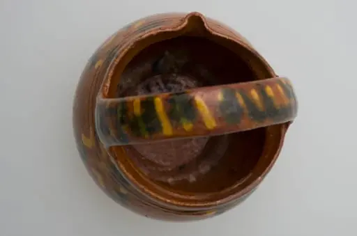 Vas de mici dimensiuni sub forma de bijou; pântecos cu gâtul scurt și gros, gură răsfrântă și cioc. Smălțuit în interior și la exterior. În partea superioară se află două linii incizate. Pe corp avem motive florale stilizate, iar pe mănușă decor geometrice: liniar și punctiform. Diametral, peste gură aven o mânușă aproximativ la fel de înaltă ca vasul. Cromatică: fond: cărămiziu; motive: galben, verde.