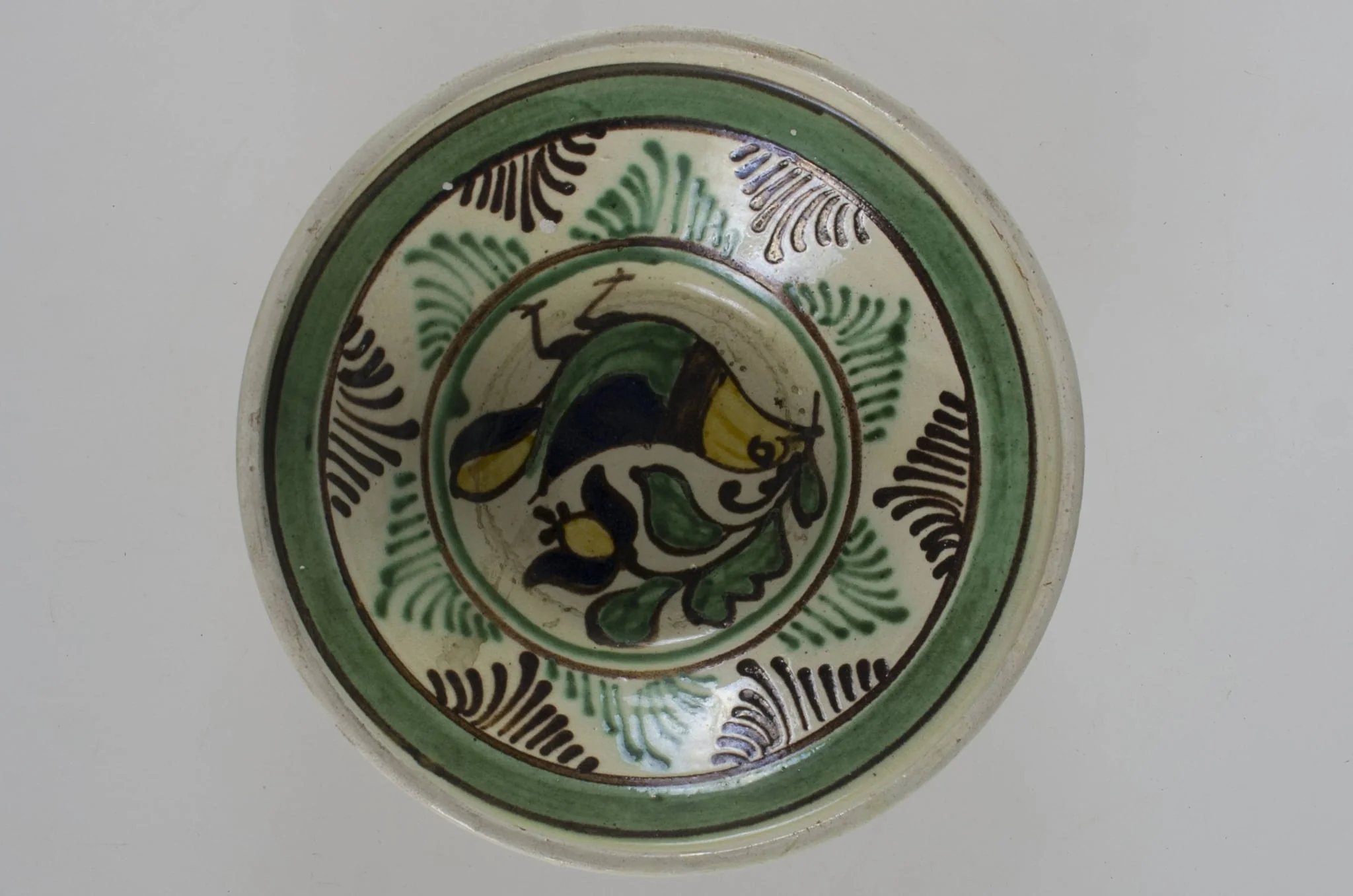 Blid de formă tronconică, adâncit, cu buza înălțată și ușor evazată. Este smălțuit în interior și în exterior (buza). Decorat la interior cu motive avimorfe și fitomorfe, încadrate de două cercuri concentrice; pe margine, în interior este decorată cu linii și brăduț stilizat, iar în exterior cu două linii; pe fund are două găuri pentru agățare. Cromatică: fond: gri (exterior); alb (interior); motive: maro; verde; galben; negru., by Pall Antal