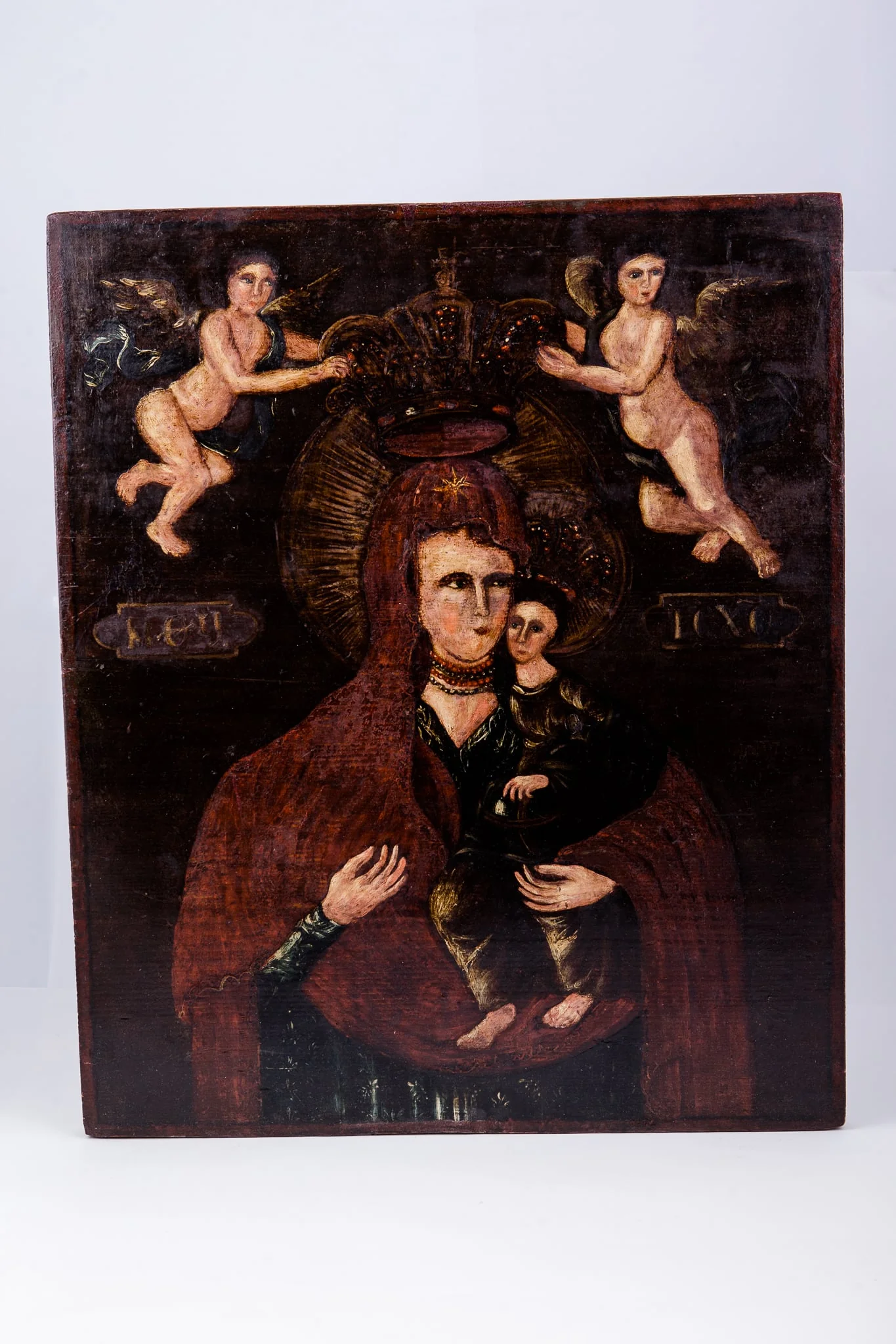 Maica Domnului ține în brațe Pruncul Iisus Hristos, care arată cu mâna dreaptă înspre Maica Domnului, prezentându-ne-o. Maica Domnului este înveșmântată în mantie cu maforion roșu-stacojiu, cu interiorul negru. Maica Domnului are aureola în raze luminoase de soare. Pruncul Iisus Hristos este înveșmântat cu sacos și omofor brun spre negru, cu coroană și aureolă pe cap. Fondul icoanei este negru întunecat, în contrast fiind cu lumina chipurilor și cromatica veșmintelor. În registrul superior sunt doi îngeri îndreptați spre coroana stilizată a Maicii Domnului, făcând gestul Încoronării. Îngerii sunt pictați asemenea unor putti, din pictura barocă. Cromatică este armonioasă: roșu stacojiu, brun, acajou, brun-ocru, brun, bej, alb, verde-olive, negru. Inscripția din româno-chirilică se traduce MP IC XC Maica Domnului Iisus Hristos. Icoana este pictată în manieră barocă și are atmosfera catolică.