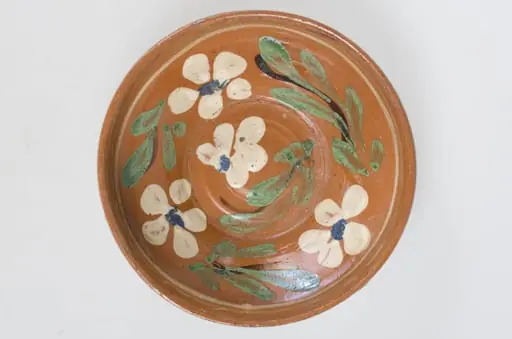 Blidul de formă tronconică adânc, smălțuit (la interior). Acesta este ornamentat cu motive florale, având cu buza înaltă. Blidul este neornamentat la exterior, fiind smălțuit (la exterior) doar pe buză. Pe exteriorul buzei este incizată o linie. Fundul obiectului are formă circulară, fiind prevăzut cu două orificii pentru prindere. Cromatică: fond: cărămiziu (exterior); alb (interior); decor: verde; alb; albastru; maro.