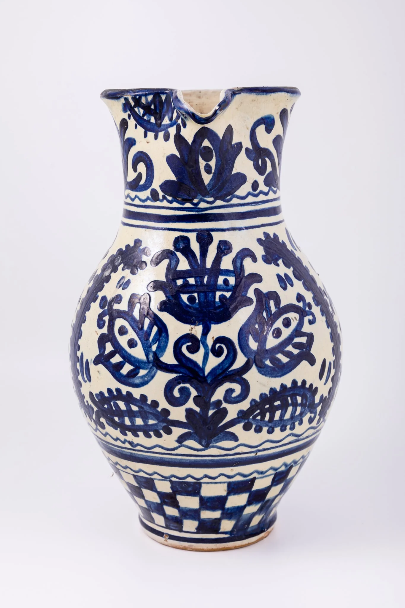Cană piriformă prevăzută cu o toartă dreaptă și lată, gura rotundă, prevăzută cu cioc de scurgere. Suprafața decorativă a vasului este împărțită în patru registre decorative. Primul registru dispus pe gâtul piesei prezintă un decor floral și fitomorf reprezentând lalele și lujeri. Al doilea registru prezintă o linie vălurită și trei linii subțiri circulare. Decorul central, reprezintă trei „arbori ai vieții” stilizați realizați din trei lalele mari, înflorite, lujeri și frunze, separați de câte o semilună. Registrul al patrulea prezintă motivul tablei de șah. Deasupra toarte pictate cu motive florale și fitomorfe este redat anul confecționării piesei: 1980, iar pe fundul vasului numele persoanei care a pictat piesa: Herta Wilk. Cromatica: alb, albastru-cobalt.