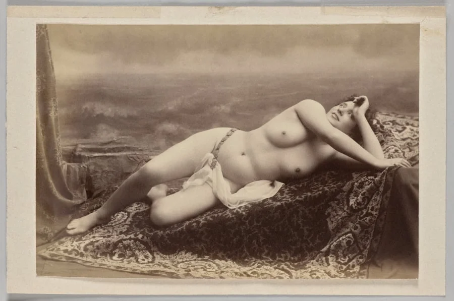 Untitled (reclining nude on carpet against painted backdrop of waves), by Unknown, 1874
