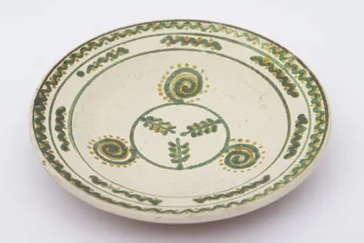 Vas ceramic de formă rotundă și profil tronconic aplatizat cu pereții larg evazați. Fața farfuriei a fost introdusă în angobă albă, decorația a fost făcută cu pensula. Pe fundul vasului sunt trei crengi de brad circumscrise. Pe pereți au fost pictate trei spirale punctate. Buza a fost împărțită în două registre: primul cu șapte valuri întrerupte; al doilea val continu, punctat. La posterior, baza este perforată pentru atârnare și incizată inscripția ,,D. Șchiopu''. Cromatica: fond: motive: verde, galben.