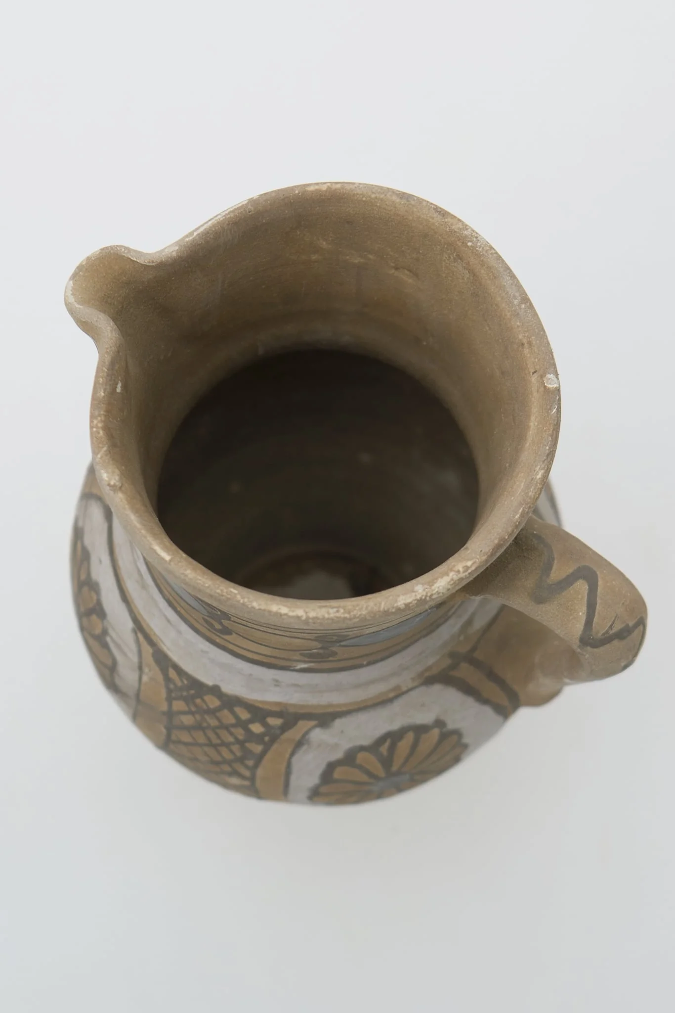Cană de vin de formă bitronconică cu gâtul lung și buză dreaptă cu cioc. Registrele ornamentale se succed de jos în sus, delimitate de cercuri concentrice, și prezintă pe corpul vasului motive florale și geometrice sub formă de hașură întrerupte de partea de sus de o zonă cerc alb mai gros și mai apoi continuat cu cercuri concentrice ce delimitează de mijloc și de sub buză două cercuri albe groase (angoba). Cromatică: fond: alb; cărămiziu; motive: maro; gri; albastru.