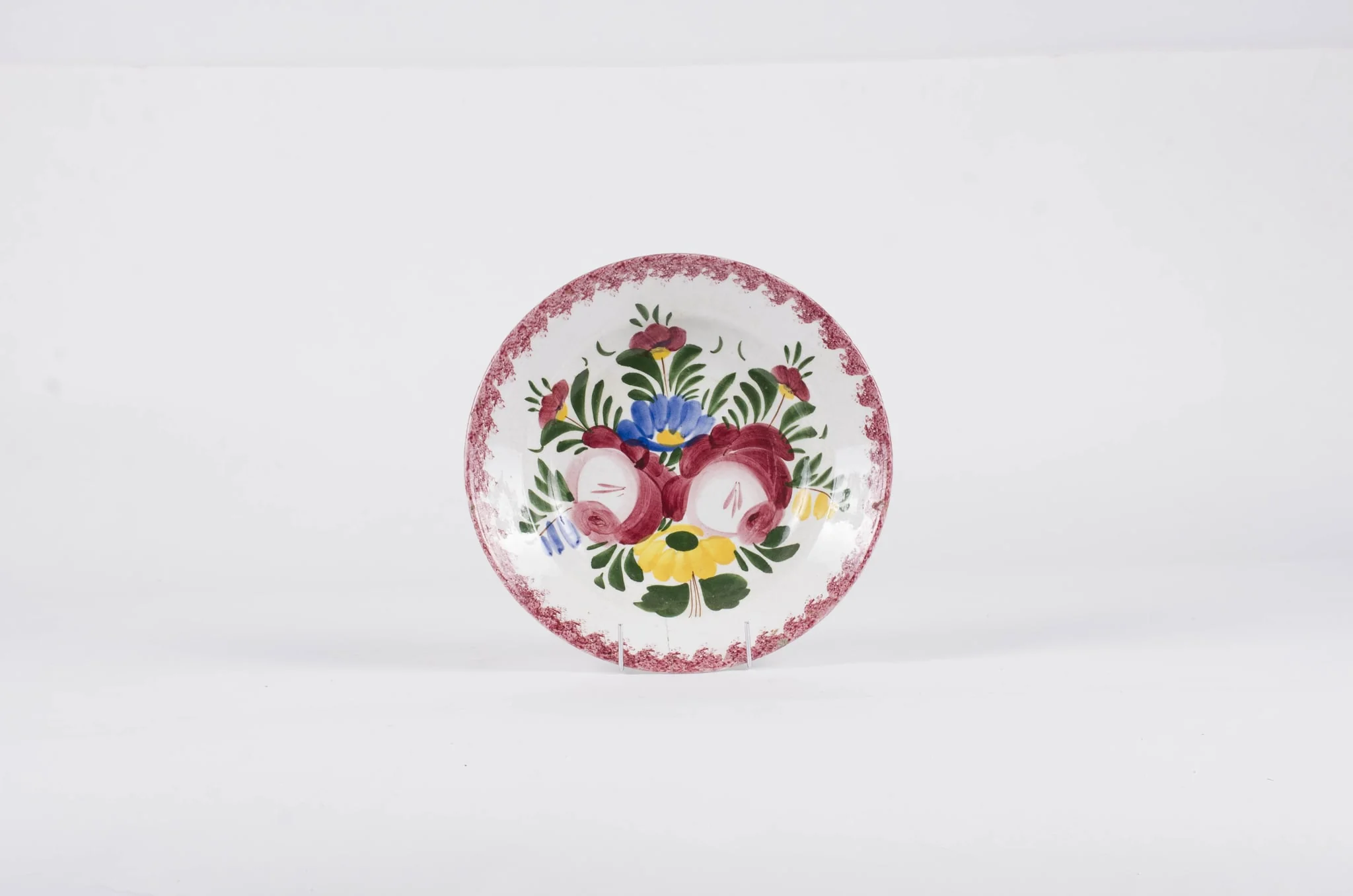 Vasul este de formă tronconică fiind smălțuit interior-exterior. Este confecționat din faianță Decorul este format din motive florale pictate pe fond alb; gura este decorată în stropi de culoare vișinie iar baza farfuriei este decorată cu motive florale. Se identifică șapte flori alcătuind motivul decorativ pe baza farfuriei. Pe spate inscripția este indescifrabilă. Cromatică: galben; albastru; verde; vișiniu; alb;, by Unknown, 1850