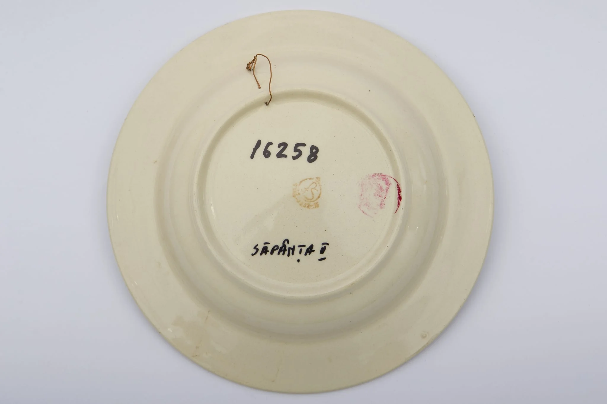 Piesă ceramică smălțuită, de formă circulară, cu baza plată, pereții puțin înălțați și marginile larg evazate. Peste stratul alb de angobă a fost pictat decorul fitomorf stilizat. Central, pe fundul piesei au fost realizați trei trandafiri roșii, însoțiți de patru boboci roșii și frunze verzi. Primul registru este încadrat de cel de-al doilea registru, dispus pe marginea recipientului ceramic. O bandă circulară galbeană peste care au fost realizați șase boboci roșii și frunze maro și verzi, este mărginită de două linii concentrice drepte. Farfuria era folosită în gospodărie pentru servirea hranei sau amenajarea interioarelor. Prezintă uzură funcțională. Cromatică: fond: alb; motive: roșu; verde; galben; maro., by Unknown, unspecified, 1850