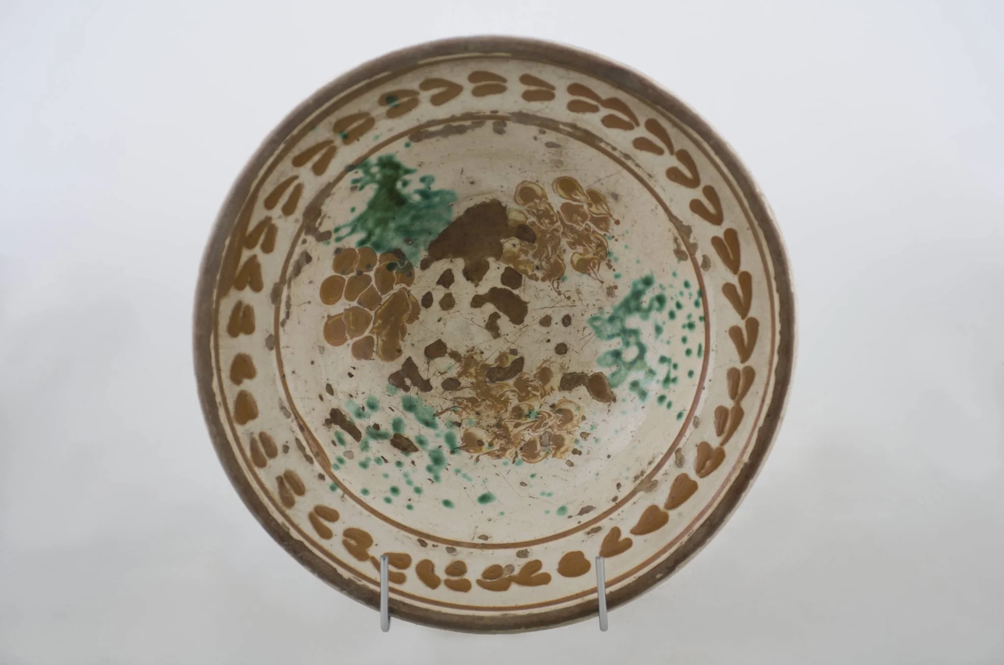 Vas ceramic de formă tronconică cu baza plată, pereții larg evazați și buza dreaptă și înălțată. După modelarea la roată, uscarea și arderea recipientului, a fost aplicat un strat de angobă în interiorul vasului, peste care a fost pictat decorul floral și vegetal stilizat, format din două registre. Primul registru, situat pe fundul și pereții vasului, și încadrat de o linie circulară, a fost decorat cu câte trei pete mari de culoare verde și galben-muștar, realizate prin stropire cu pensula. Al doilea registru, cel care decorează buza recipientului ceramic și este mărginit, la rândul lui de o linie circulară, prezintă elemente ornamentale de tipul „bobului de grâu”. Cromatică: fond: alb; motive: roșu; albastru; verde., by Unknown, unspecified, 1850