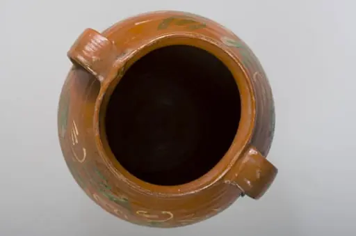 Vas de formă bitronconică, cu gât scurt cu buză rotunjită și evazată. Oala este smălțuită interior și pe 2/3 din exterior. Prezintă două toarte late ce unesc buza vasului de zona diametrului maxim. Decorații în registru floral-vegetal, dispuse concentric, în partea superioară a vasului, compuse din linii ondulate și palmate. Cromatică: fond: cărămiziu; motive: alb, verde.