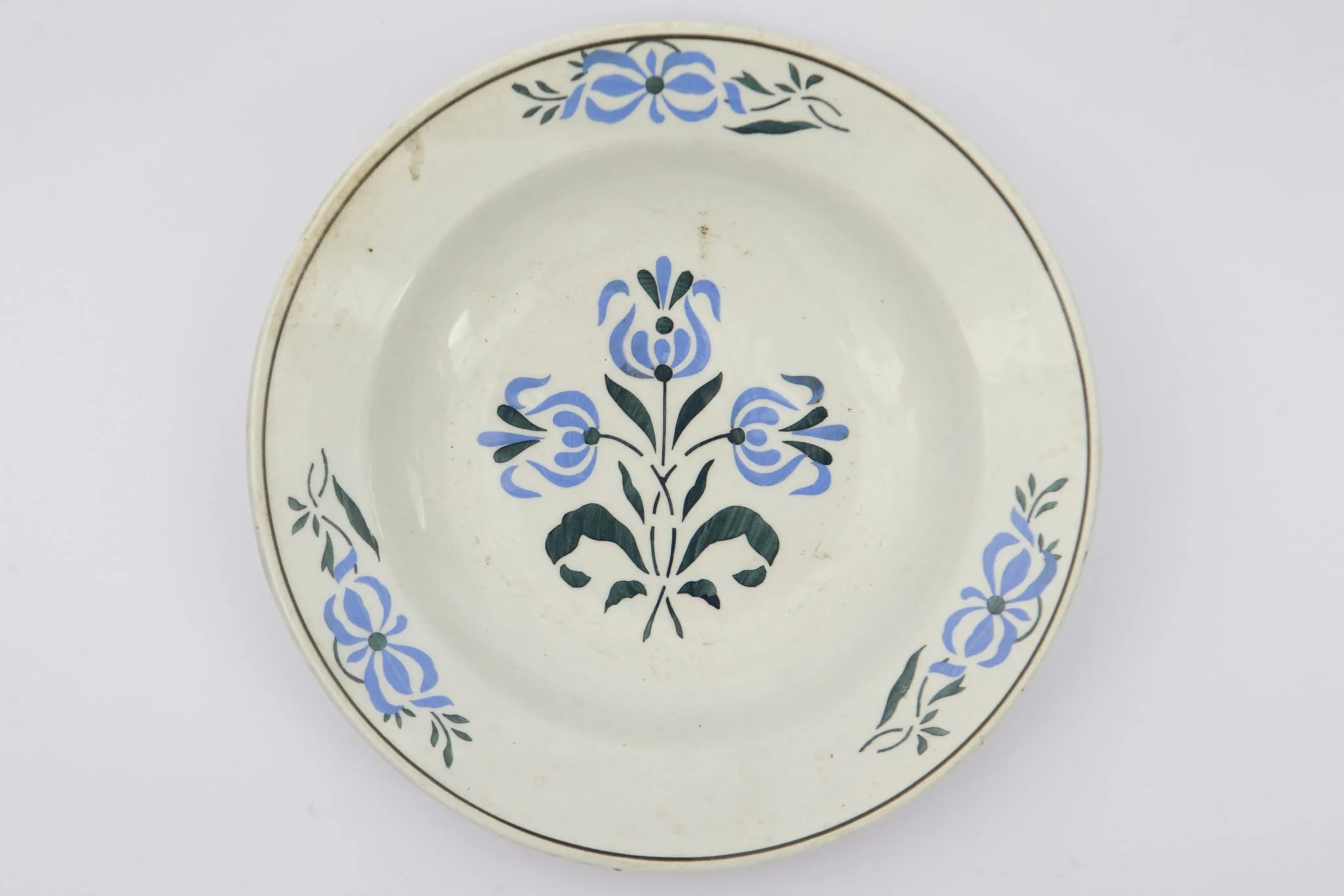 Farfurie cu fundul plat, puțin adâncit. Pe fundul vasului decor ilustrând un buchet de flori albastre cu tulpini și frunze verzi. Pe marginile vasului dispuse câte trei grupuri a două flori ca și cele de pe fund. La buză o linie neagră dispusă circular.. La posterior pe inelul de susținere practicate două perforații pentru atârnare. Cromatica: fond: alb; motive: albastru, verde, negru.