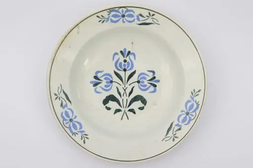 Farfurie cu fundul plat, puțin adâncit. Pe fundul vasului decor ilustrând un buchet de flori albastre cu tulpini și frunze verzi. Pe marginile vasului dispuse câte trei grupuri a două flori ca și cele de pe fund. La buză o linie neagră dispusă circular.. La posterior pe inelul de susținere practicate două perforații pentru atârnare. Cromatica: fond: alb; motive: albastru, verde, negru.