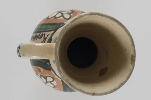 Cană cu gât lung, cu buza evazată și o toartă. Este smălțuită în interior și în exterior. Prezintă decor pe toată suprafața cu motive fitomorfe, motive florale stilizate și motive geometrice: linie, linie ondulată, punct, tablă de șah. Pe toartă scrie ”Jozsa Janos”, iar pe corp, chiar lângă toartă, scrie ”Korond 1974”. Cromatică: fond: alb; motive: bej, maro, verde, negru.