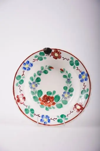 Farfurie de porțelan smălțuită pe fond alb. Decorată cu flori și frunze dispuse sub formă de ghirlande atât în centrul vasului cât și pe buza acestuia. De asemenea sunt prezente și motive geometrice: linia și linii întrerupte. Comatică: fond: alb; motive: verde; albastru; galben; roșu.