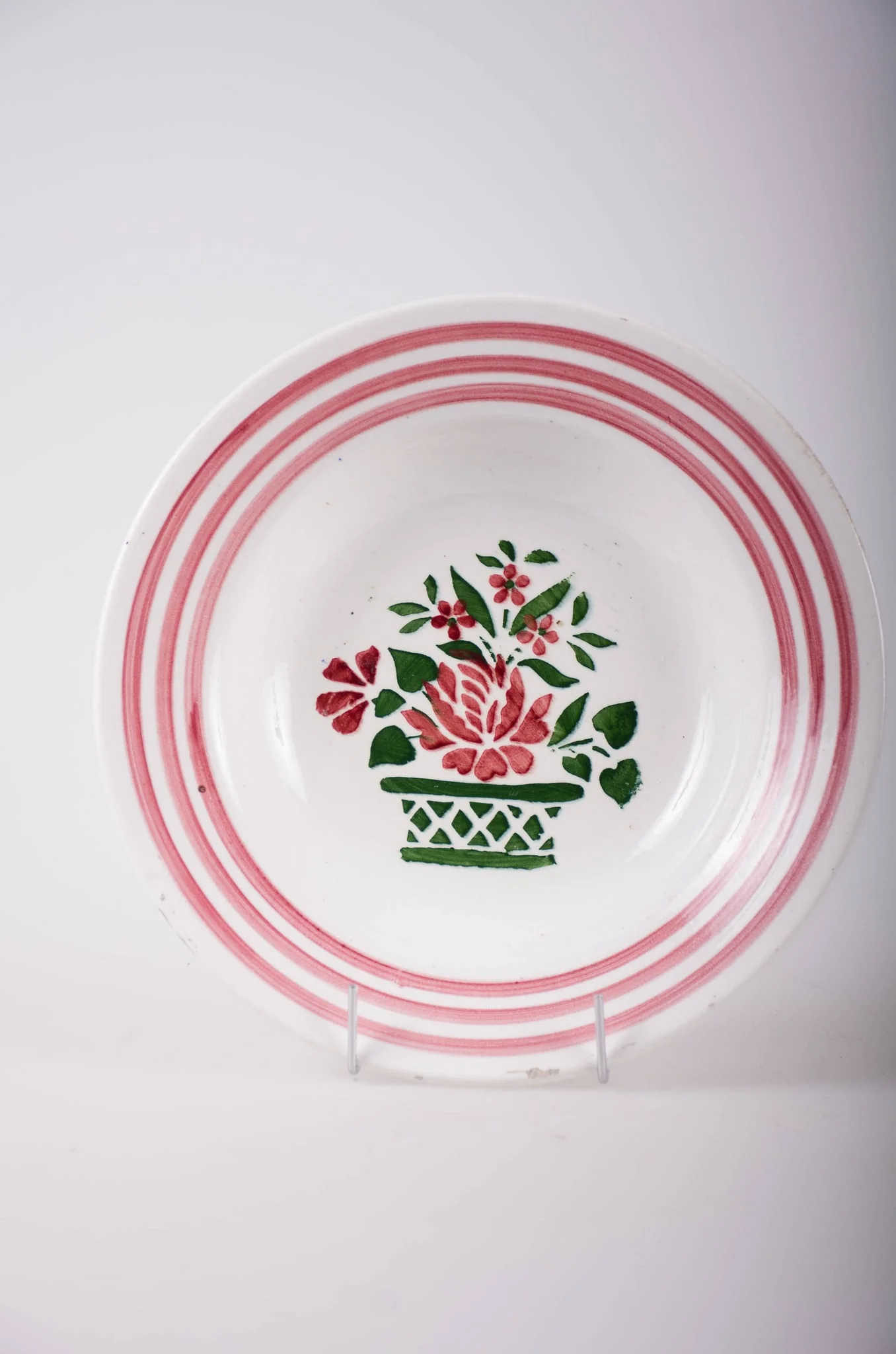 Vas de formă tronconică, adâncit; pe fund are găuri pentru agățare. În centru este decorată cu motive florale: vază cu flori; pe margine sunt trei cercuri concentrice; motive geometrice: linie, romb, triunghi. Pe fund are o marcă indescifrabilă. Cromatică: fond: alb; motive: vișiniu; verde.