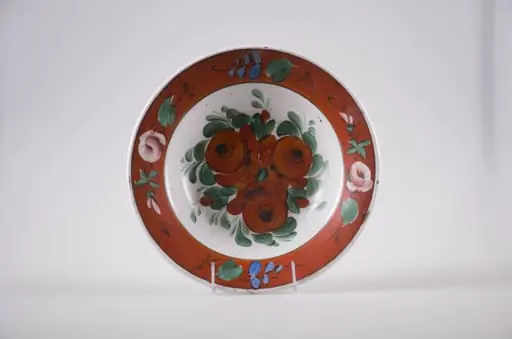 Farfurie de formă tronconică din faianță, cu buza dreaptă, ornamentată prin pictare. Fundul este alb și are pictate trei flori roșii înconjurate de frunze mărunte, este delimitat de buza farfuriei cu o linie subțire, neagră. Buza vasului este roșie, decorată cu flori roz și frunzulițe discrete. În partea posterioară prezintă o gaură prin care se trece ața ce servește la agățarea farfuriei. Cromatică: fond: alb, roșu; motive: verde; roz; albastru; roșu; negru.