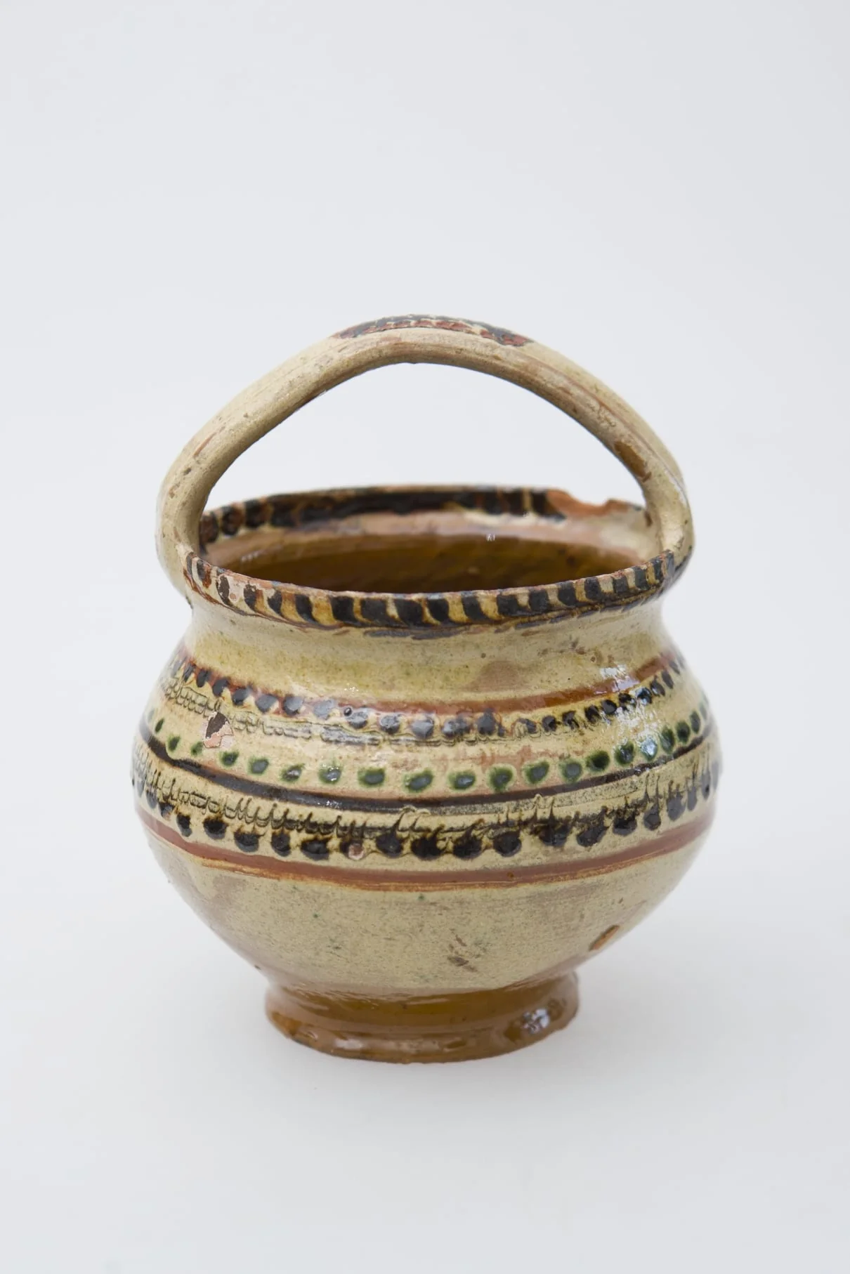 Vas ceramic de mici dimensiuni, pe bază inelară, pântecos, cu fundul și gura late. Deasupra gurii vasului a fost pusă o toartă de prindere. Buza vasului a fost pictată printr-un brâu de crenguțe. Pe pântecul vasului brâuri de puncte și două benzi subțiri jirăvite. Smălțuit în interior și exterior. Cromatică: fond: crem; motive: verde; maro; bej., by Unknown, 1850
