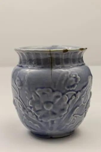 Piesă din faianță, cu aspect piriform, cu buza ușor evazată spre exterior, prevăzută cu toartă laterală semiovală. Decorul este reliefat și constă în motive florale (macul în diverse faze de dezvoltare: boboc, mac înflorit, capsule). Gâtul piesei este evidențiat printr-un brâu format din caneluri verticale. Cromatică: alb, bleu.