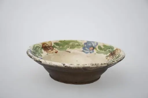 Farfurie de formă tronconică adâncă cu buza largă și decor pe fund, spre margini. Ornamentat cu motive florale. Cromatică: fond: alb; motive: maro; verde; albastru.