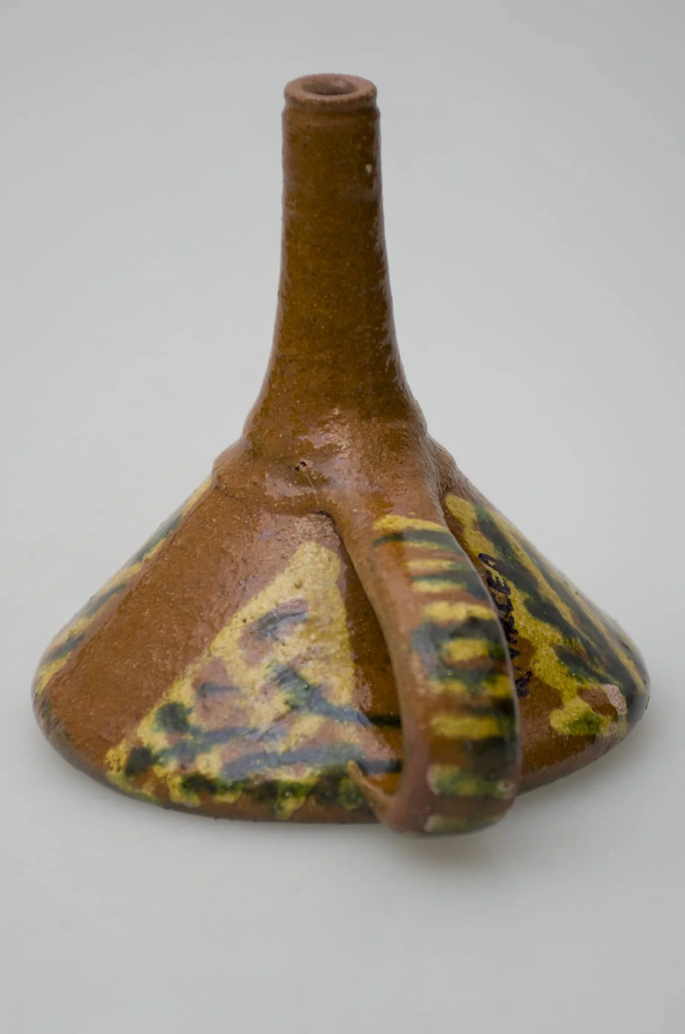 Pâlnie ceramică smălțuită, de formă tronconică, cu gura astupată cu o suprafață de lut găurită, formând o sită. La cealaltă latură a conului pâlnia este continuată printr-un tub cilindric, care se folosește la scurgerea lichidelor. Piesa de uz casnic este dotată cu un mâner care pleacă de la buză până la tubul cilindric de scurgere. Pe suprafața obiectului apar motive geometrice realizate cu pensula. Cromatică: fond: maro; motive: galben; verde., by Șchiopu Dumitru