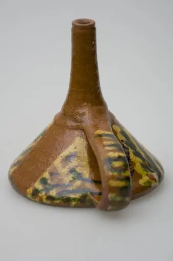 Pâlnie ceramică smălțuită, de formă tronconică, cu gura astupată cu o suprafață de lut găurită, formând o sită. La cealaltă latură a conului pâlnia este continuată printr-un tub cilindric, care se folosește la scurgerea lichidelor. Piesa de uz casnic este dotată cu un mâner care pleacă de la buză până la tubul cilindric de scurgere. Pe suprafața obiectului apar motive geometrice realizate cu pensula. Cromatică: fond: maro; motive: galben; verde.