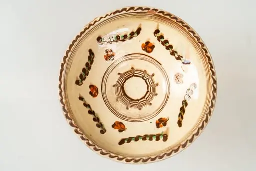 Farfurie adâncă, de tip castron, modelată la roata olarului, angobată pe fața interioară cu humă albă. Decorul este realizat prin pictare cu cornul și prin jirăvire: culorile sunt picurate cu cornul și trase (jirăvite) cu gaița. Motivele decorative sunt florale și vegetale stilizate și decor specific tehnicii prin jirăvire. Buza și bordura interioară a acesteia sunt marcate de linii concentrice sub formă de cerc. Muchia buzei este marcată de o linie continuă vălurită de culoare maro. Cromatica decorului: alb, verde, siena arsă, maro. Piesa este acoperită pe fața sa interioară de un strat de smalț transparent.
